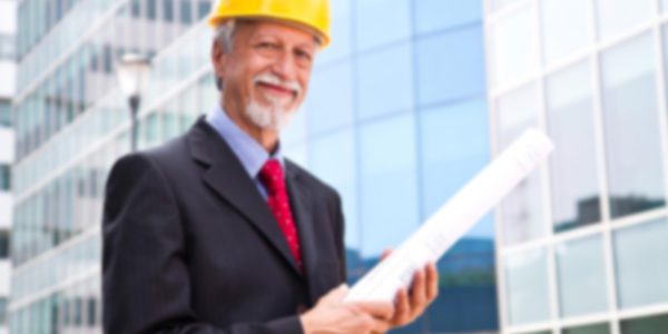 A man in a hard hat holding a blueprint in front of a building.
