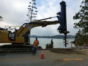 An excavator is working on a road near a body of water.