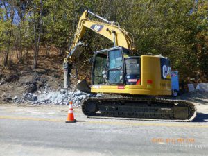 A yellow excavator is working on a road.