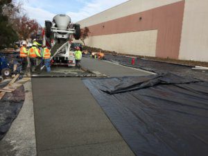 A worker is pouring concrete on a sidewalk.