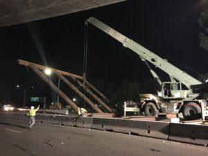 A crane lifts a bridge over a highway at night.