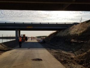 A worker is standing on the side of a road next to a bridge.