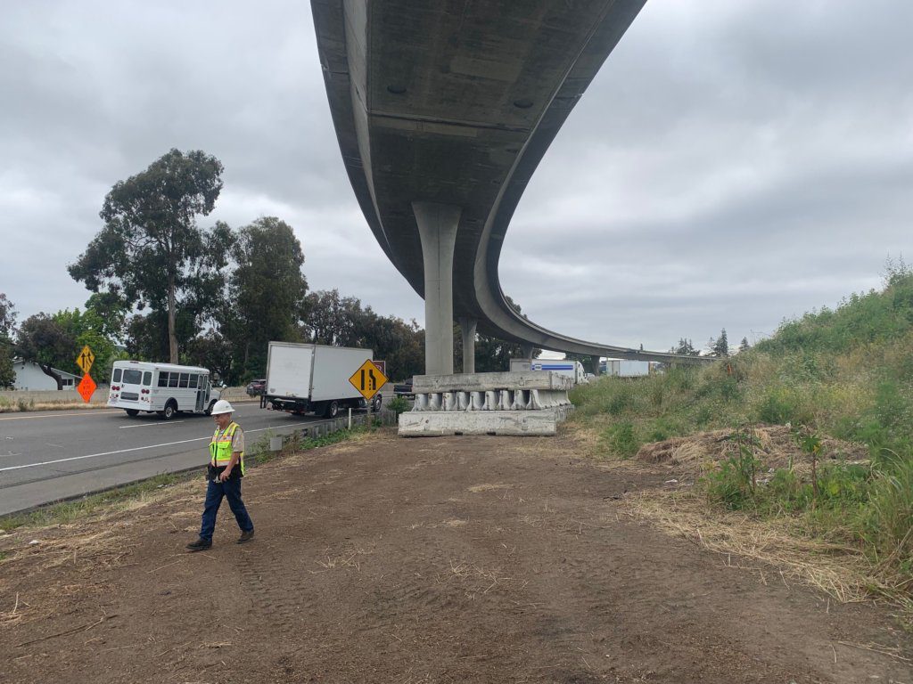A worker is standing on the side of a road under an overpass.