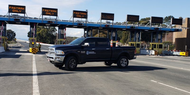 A truck is driving down the road near a toll booth.