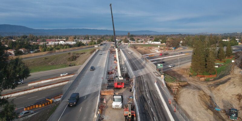 A construction site with cars and cranes on the side of the road.