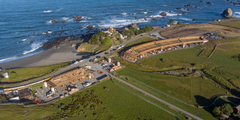 A view of the ocean from above shows a road and some buildings.