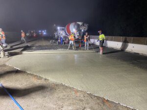 A cement truck is being poured on the side of a road.