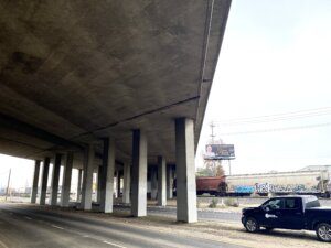 A car parked on the side of a road under an overpass.
