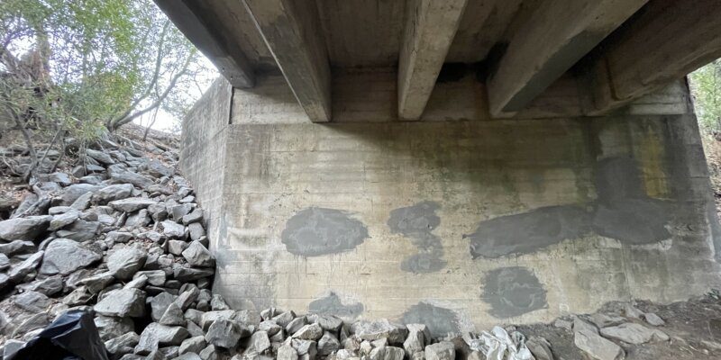 A pile of rocks under a bridge with trees in the background.